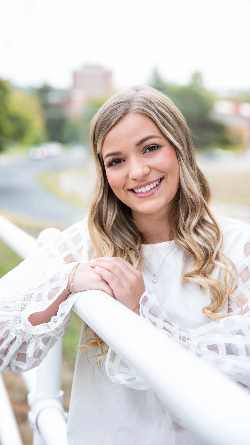 Portrait of a woman leaning against a white fence.