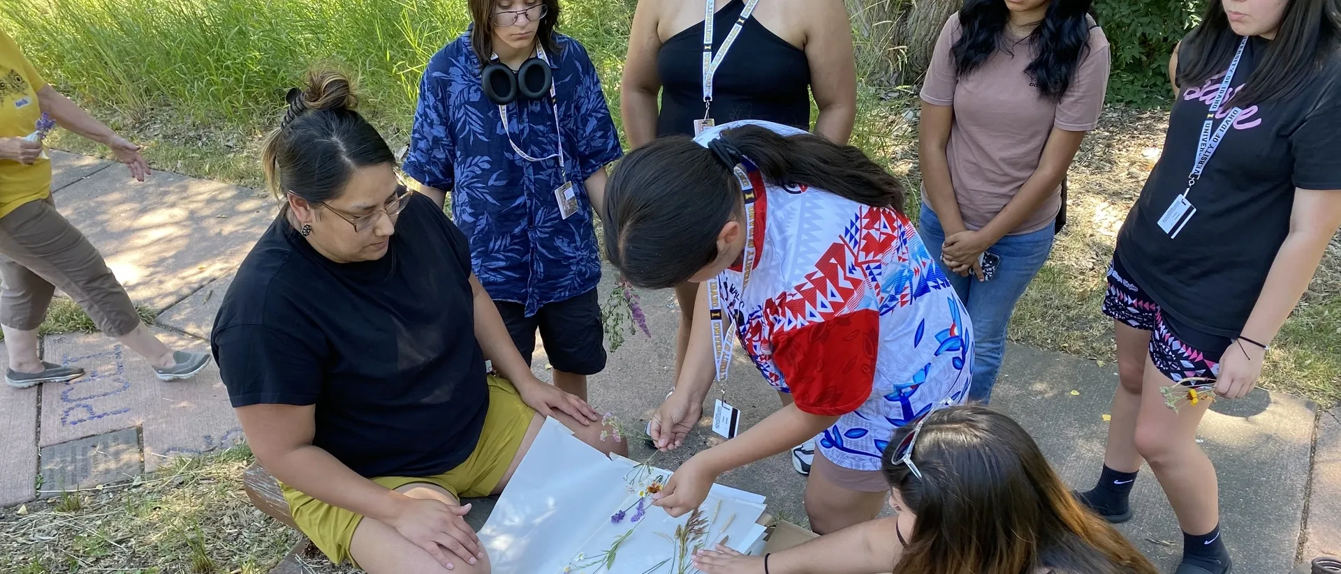 Two people sitting on bench with dried flowers with others standing around them.