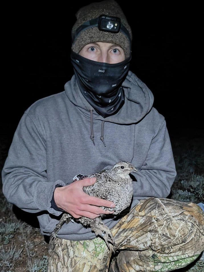 Man dressed in winter at night holds a grouse hen.