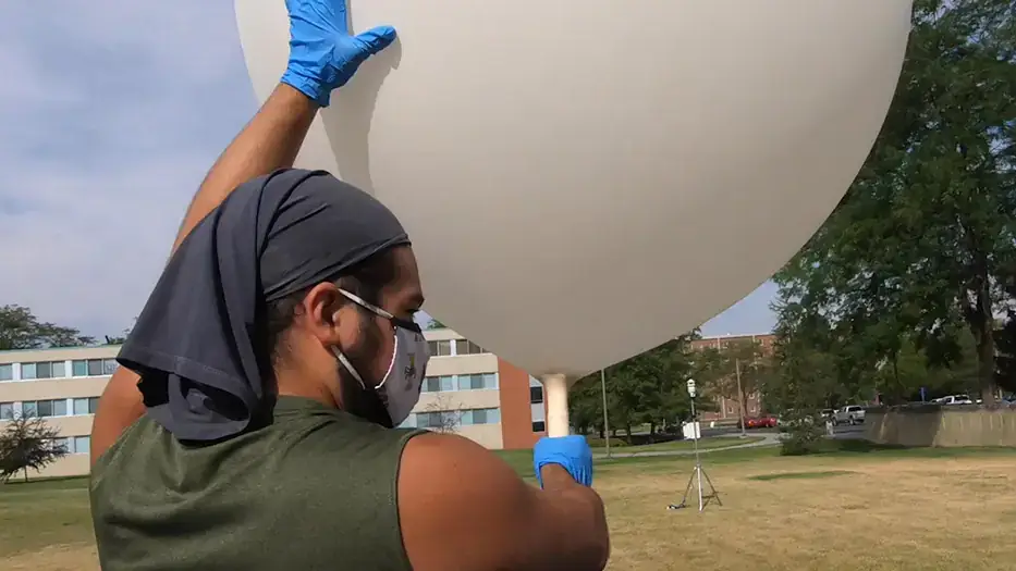 A student holds a weather balloon on the Tower lawn.