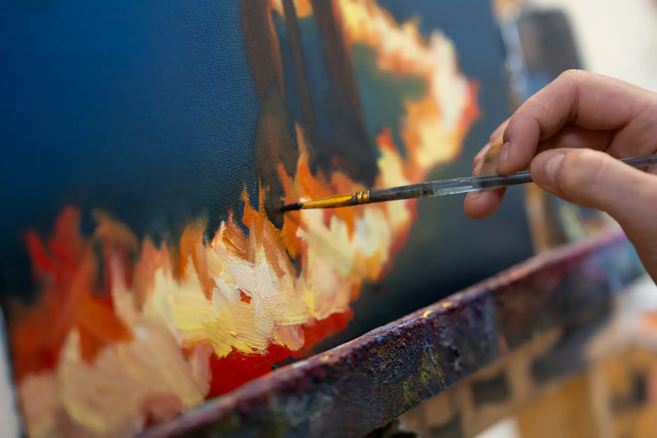 Closeup of a hand holding a paintbrush painting on a canvas.