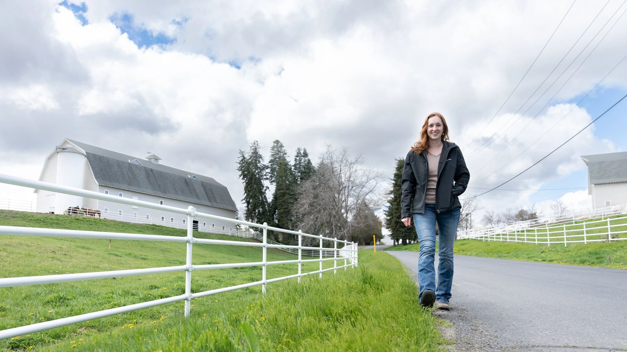 A woman waling down a road with a barn in the background.