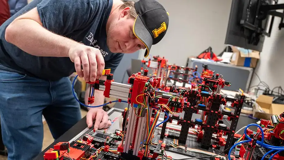 A young man in an Idaho baseball cap works with tech in a robotics classroom