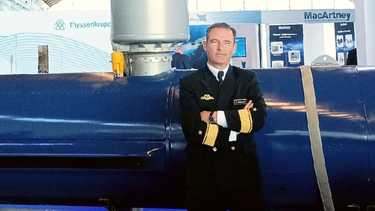 A man in a military service uniform posing for a picture in front of a blue machine.