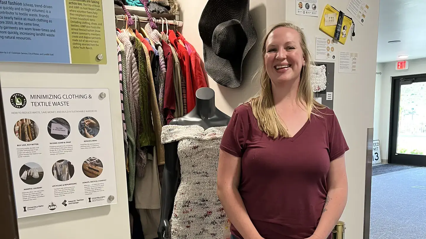 A woman poses by an exhibit featuring a model kitchen, using recycled and reused materials.