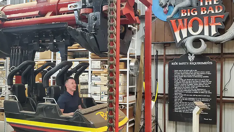 A man sits in a demonstration model of a rollercoaster car