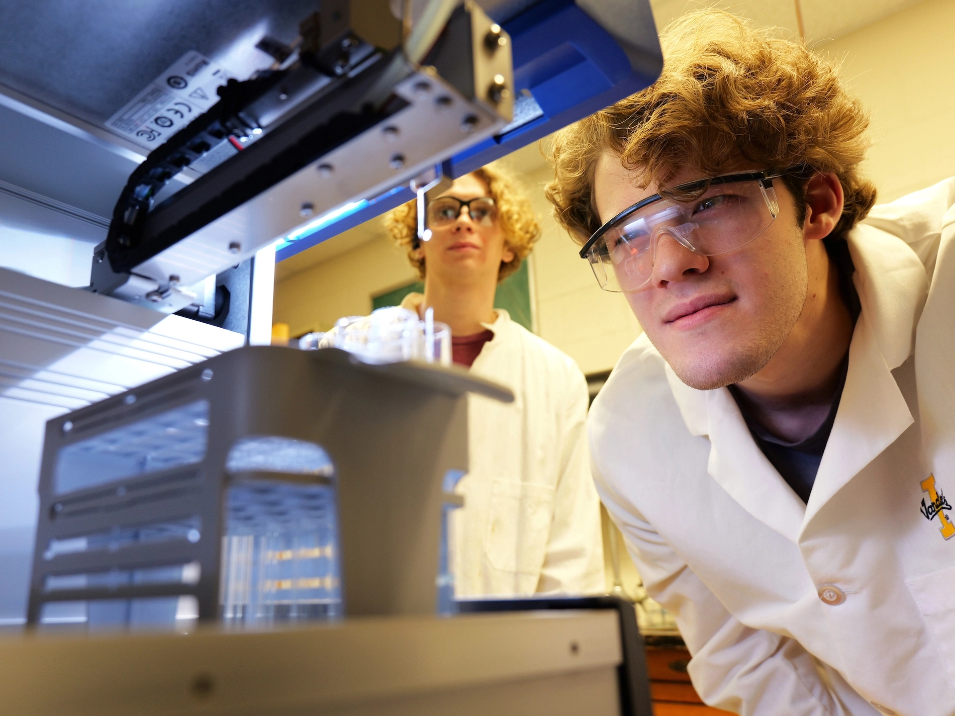 Two students in lab coats examining a research machine