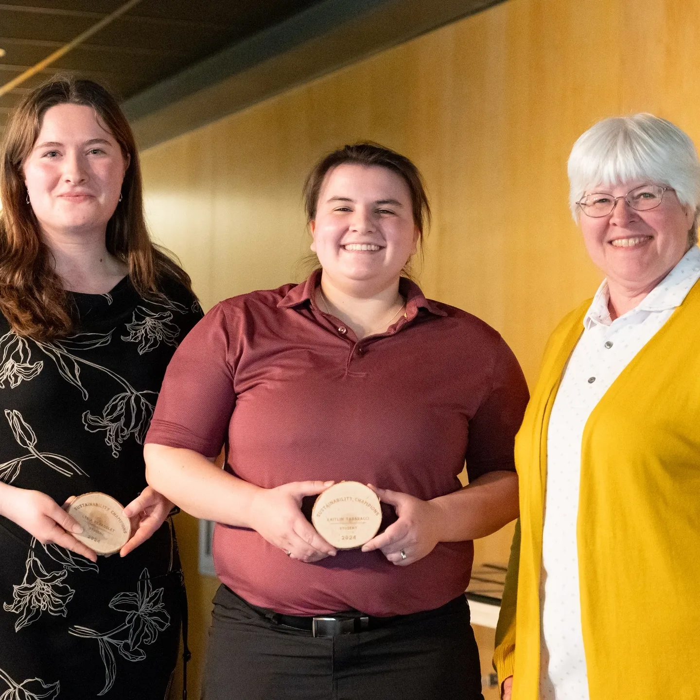 Three woman standing next to each other, with two of them holding an award.
