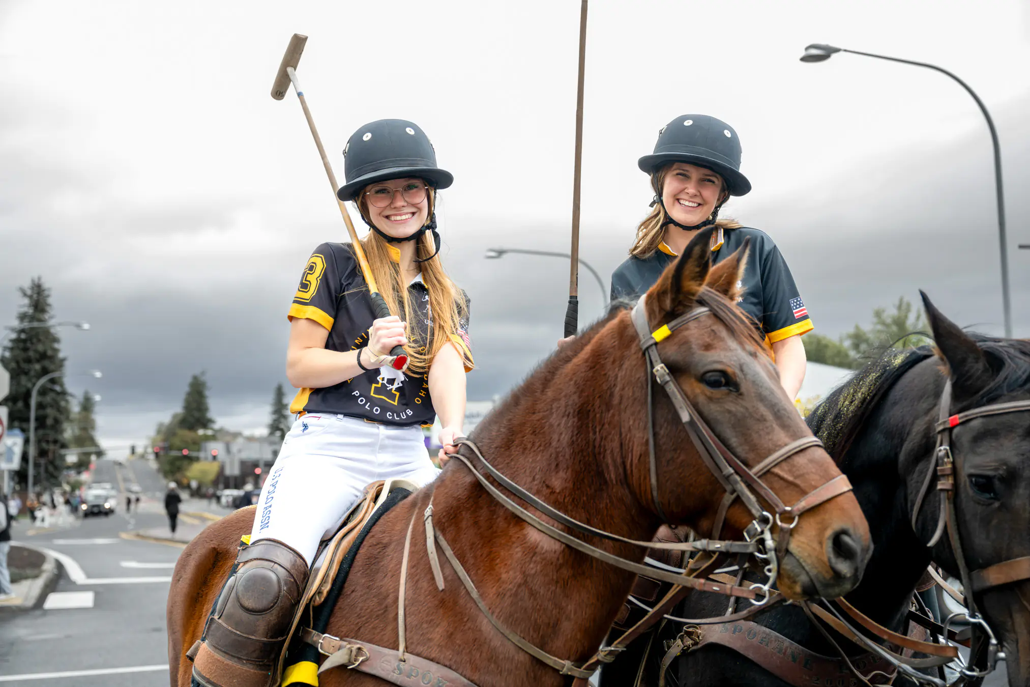 Two female students in polo uniforms, riding horses.