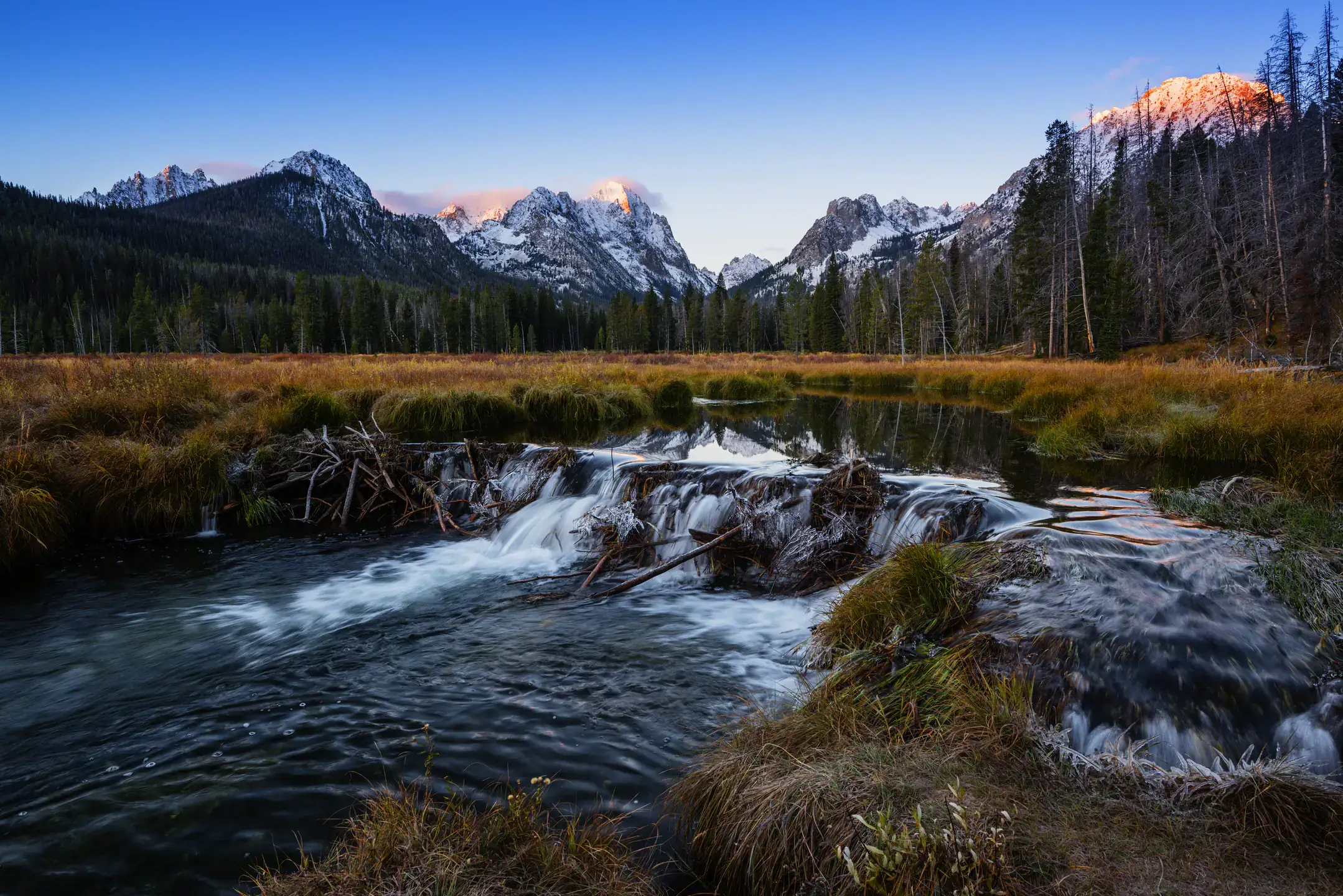 Beautiful snow covered Sawtooth mountain range reflecting in calm waters of a mountain lake or a beaver dam on a fine autumn morning in Stanley, Idaho, USA
