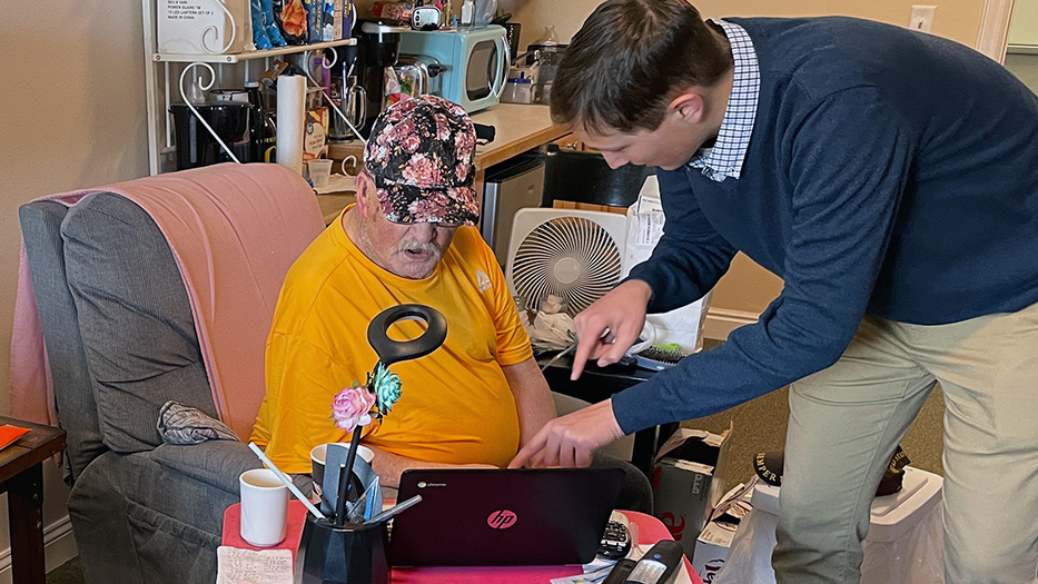 A young man showing an elderly man something on his laptop.