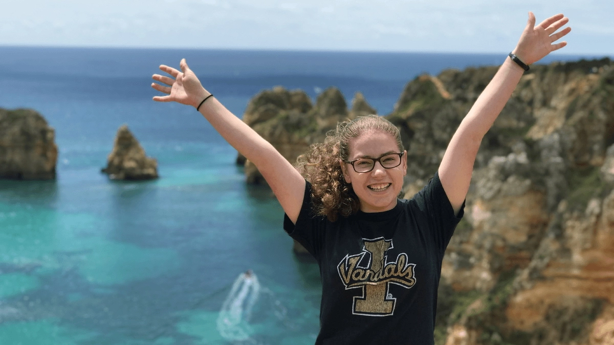 A woman smiling with her hands up standing in front of the ocean