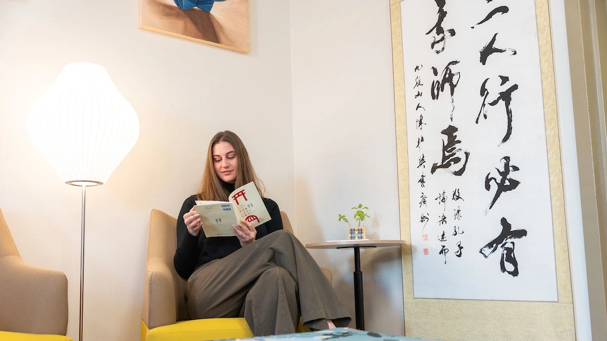 Megan Lolley sits in a lounge reading while surrounded by Asian art.