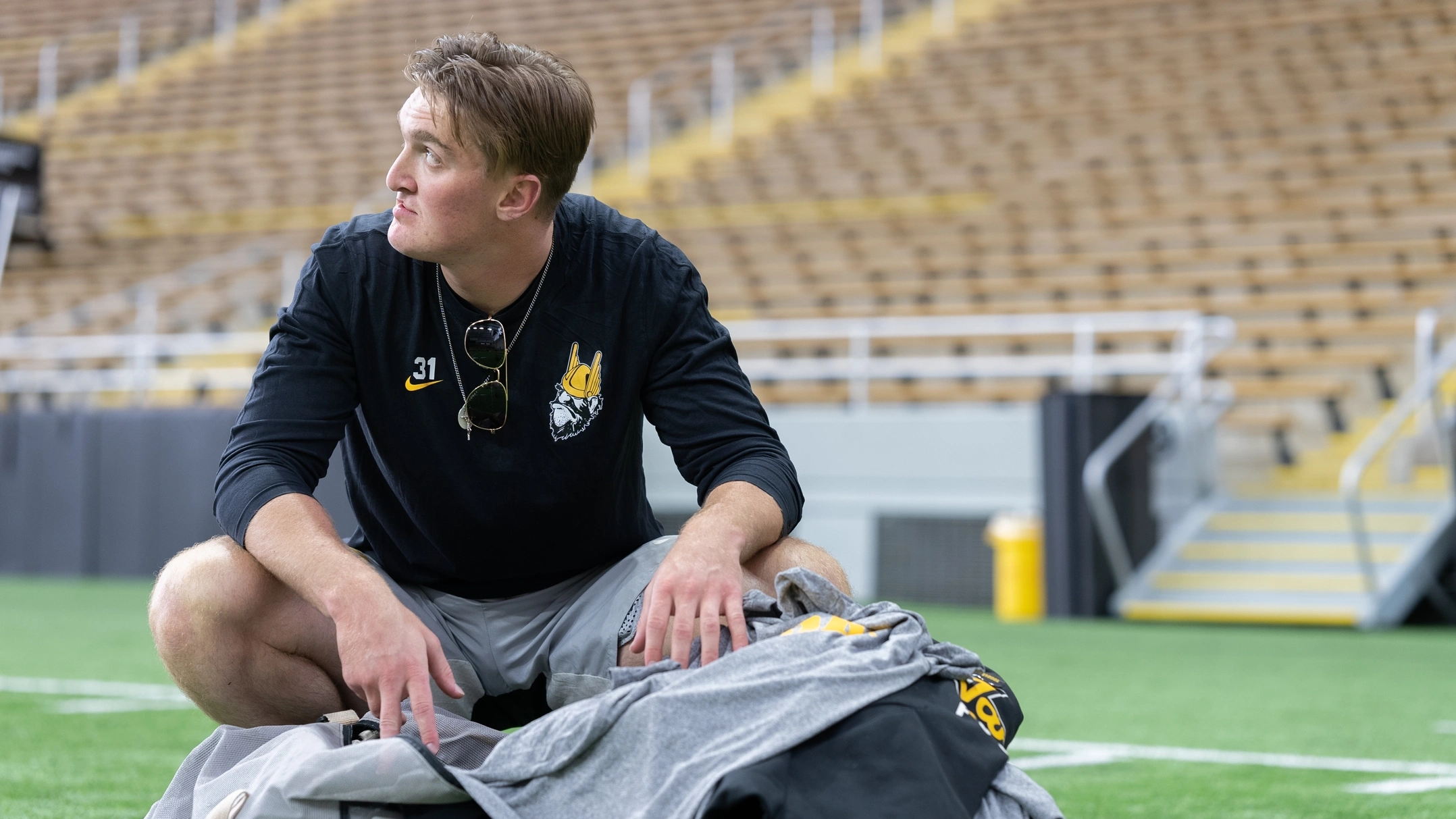 Football layer in light practice gear kneels on field with his pads and helmet and looks skyward