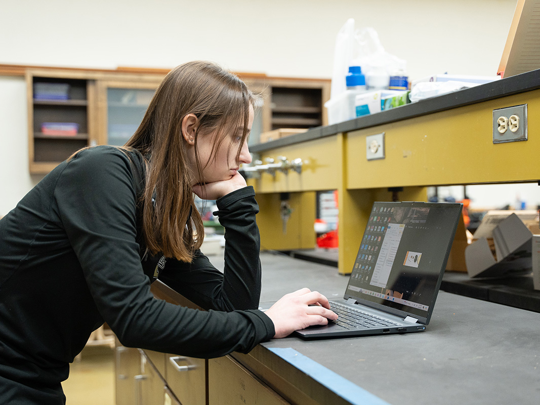 Woman in a lab leans over a laptop.