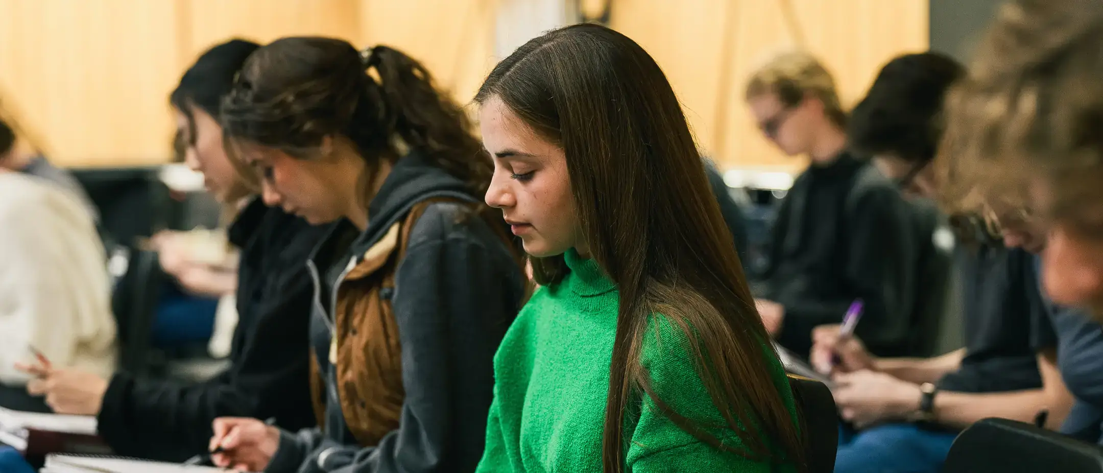 A student writing in a textbook while sitting in a classroom.