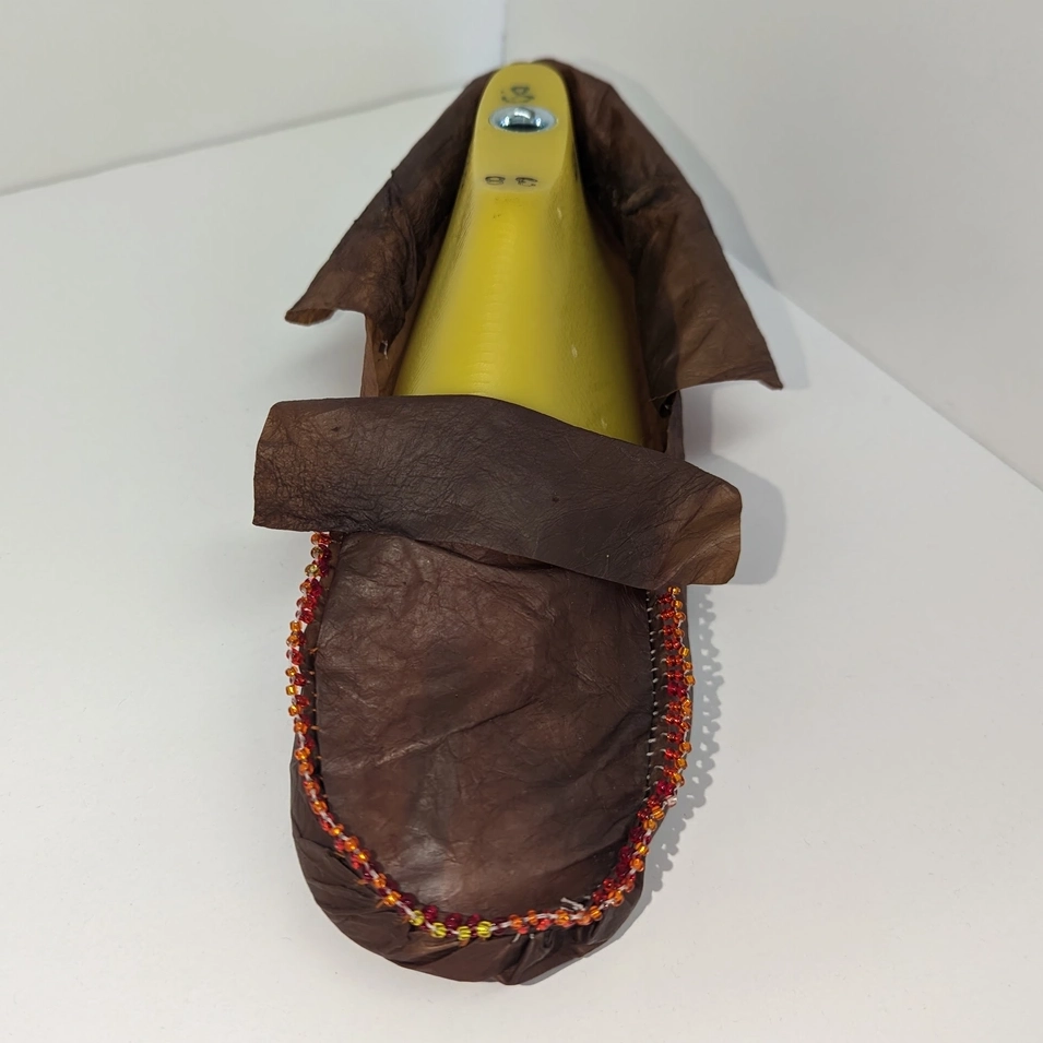 A dark brown SCOBY moccasin with beading sits on a table