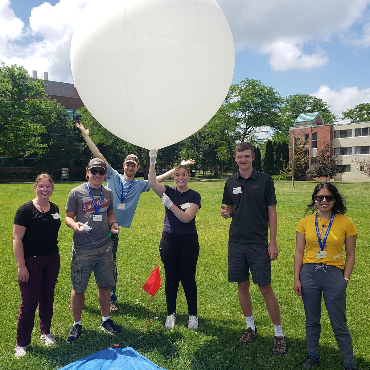Six people stand on a lawn with a big white weather balloon.
