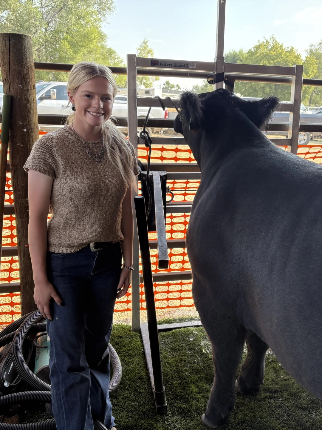 A girl with long blond hair poses with a large black steer.