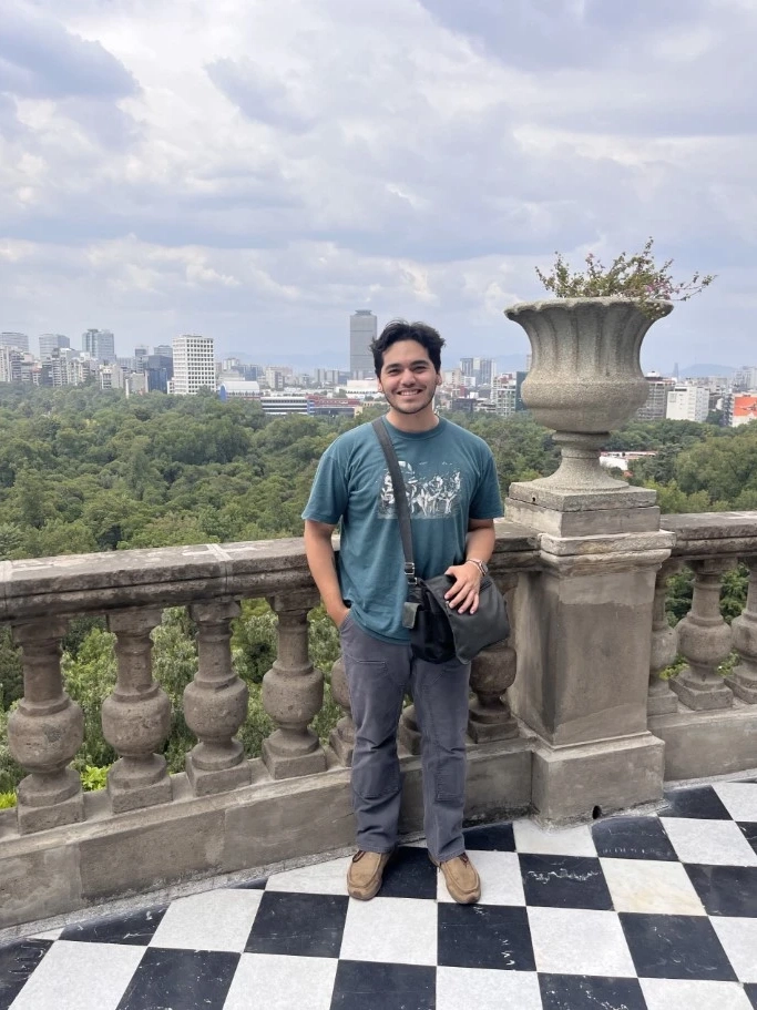 Alex standing on a balcony with trees and the cityscape behind him.