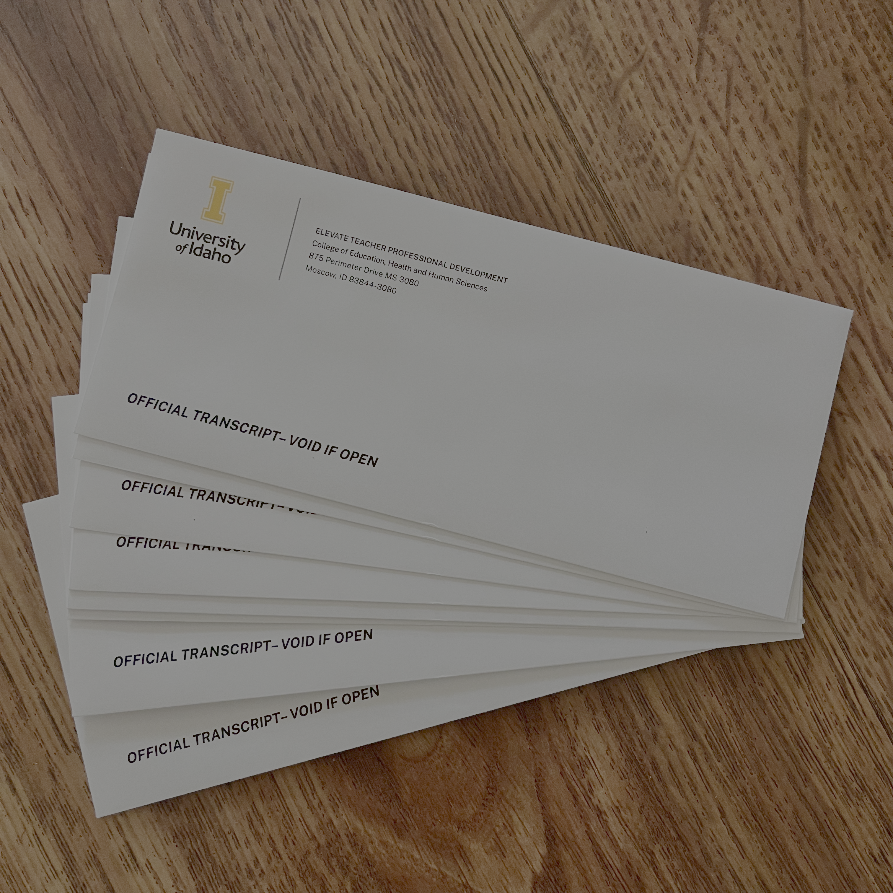 A stack of official transcript envelopes from the University of Idaho labeled 'VOID IF OPEN,' placed on a wooden surface.