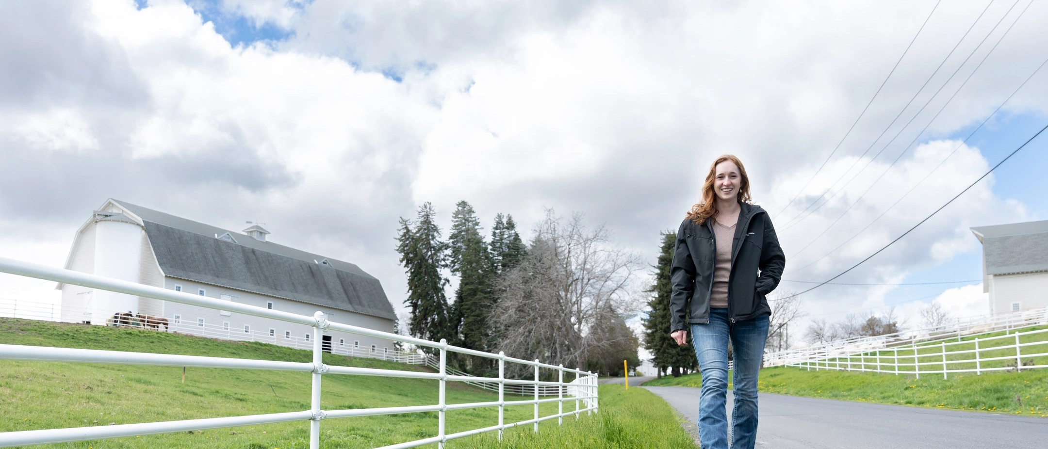 A woman walking down a road with a barn in the background.