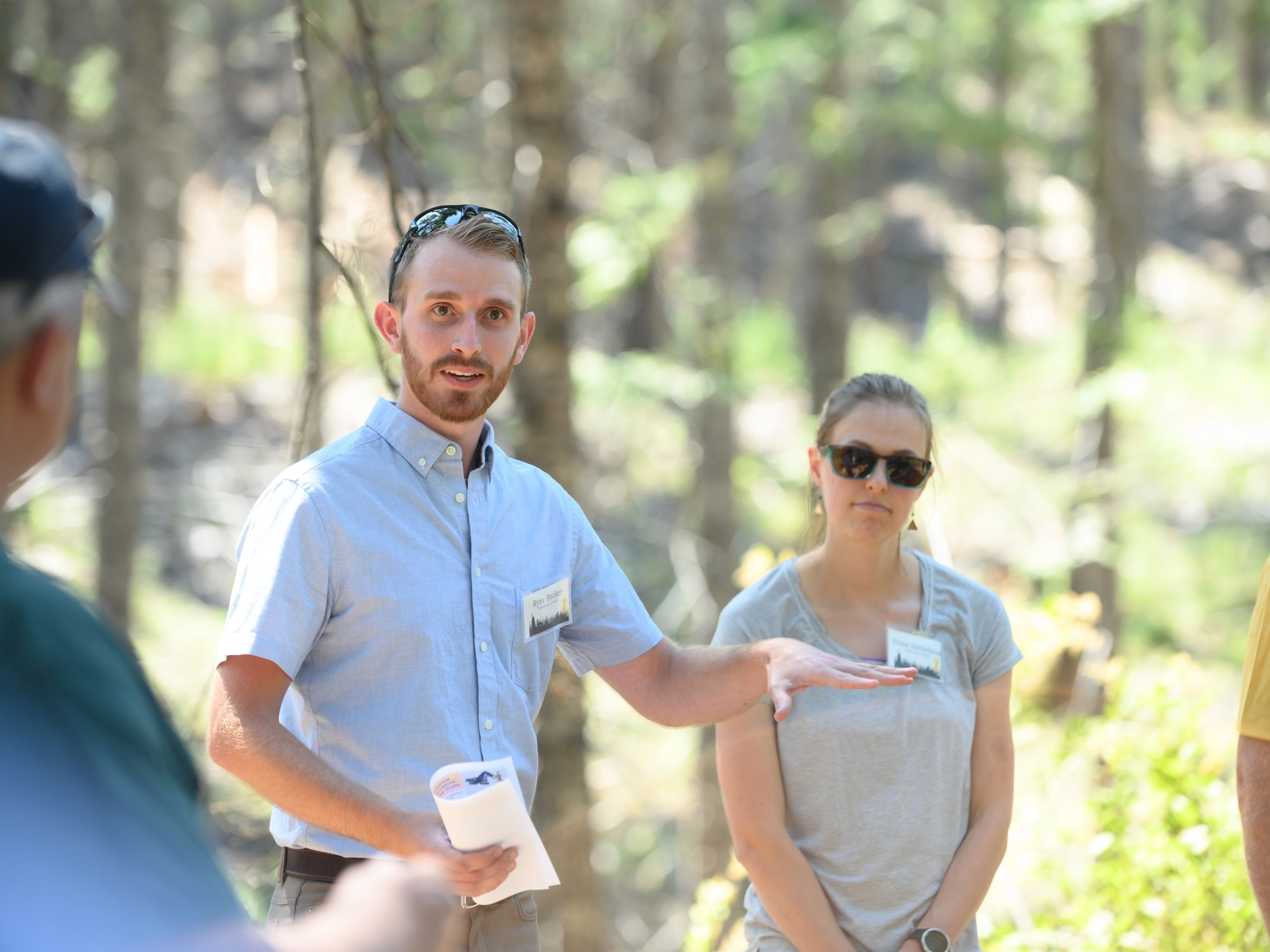 A group of people standing in a circle in the woods, discussing forestry.