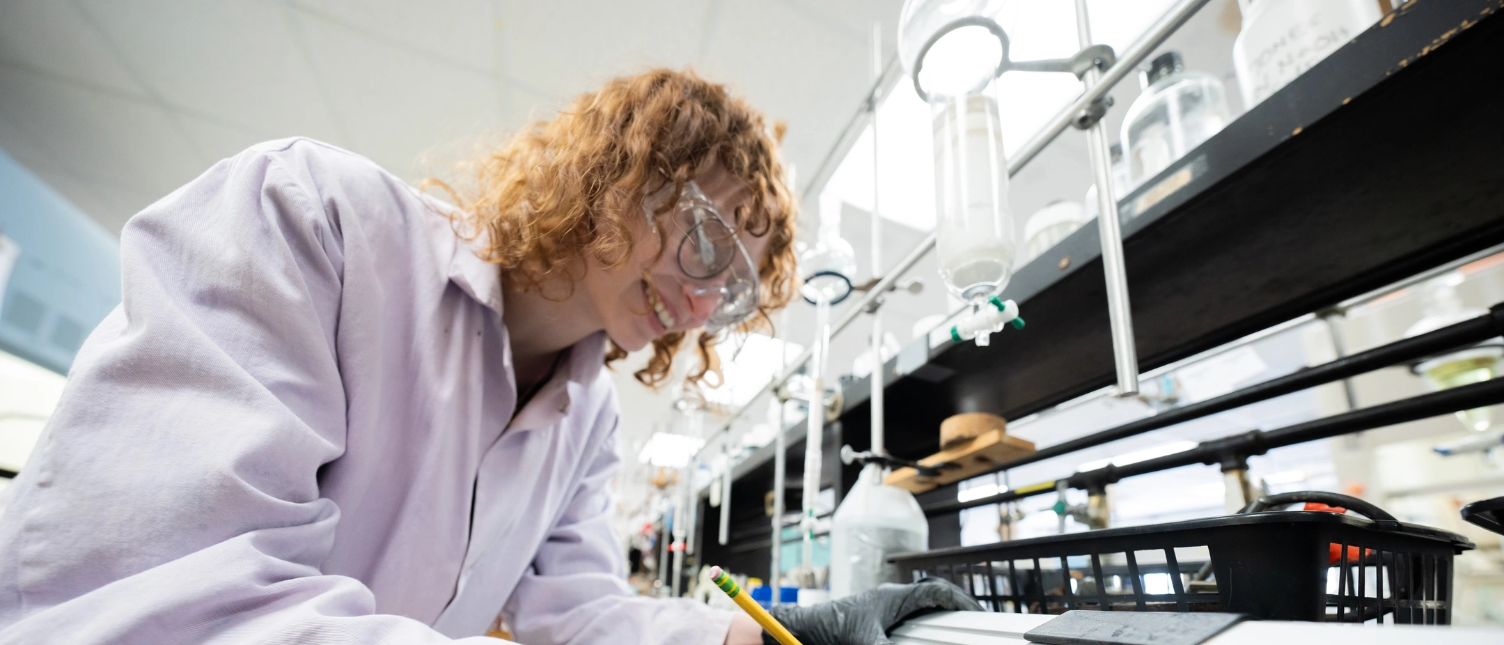 Student in a lab coat and goggles writing labels in chemistry lab