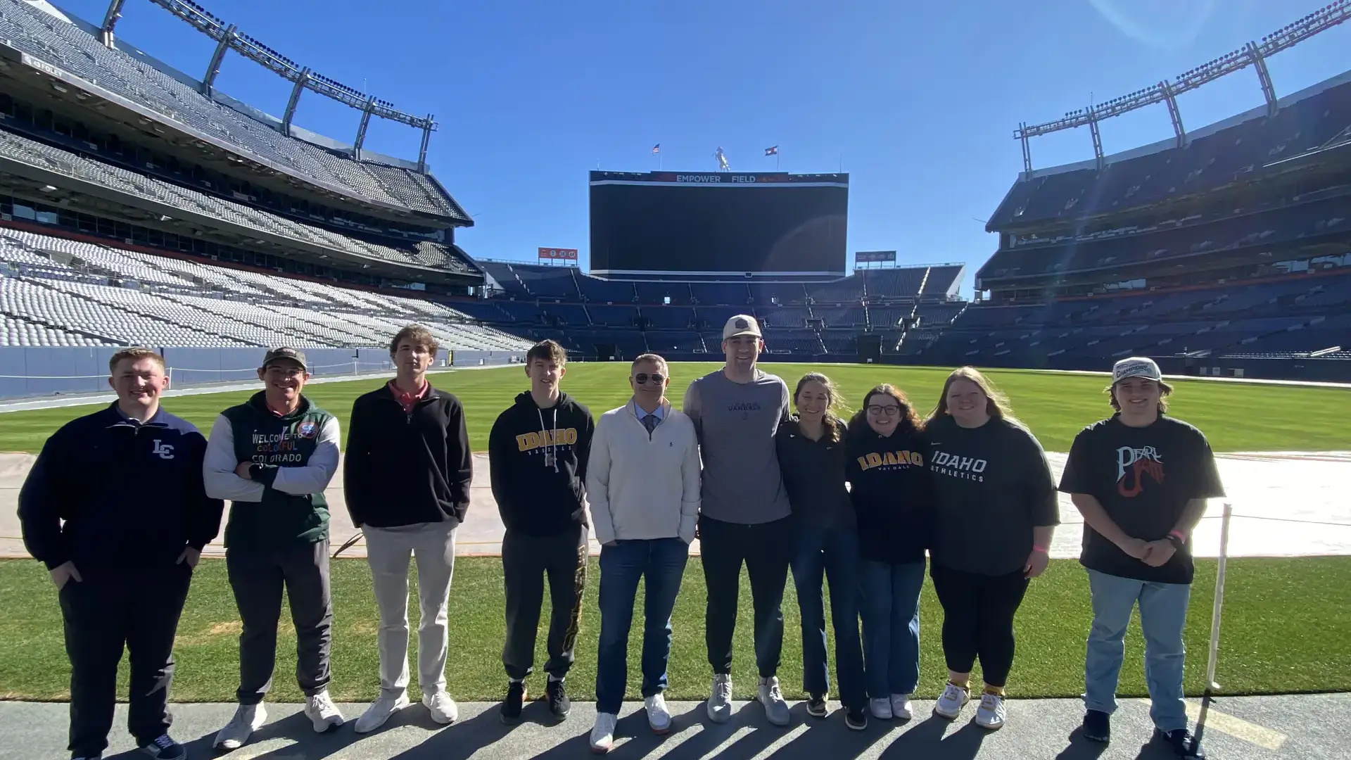 Ten people stand on the Denver Broncos field.