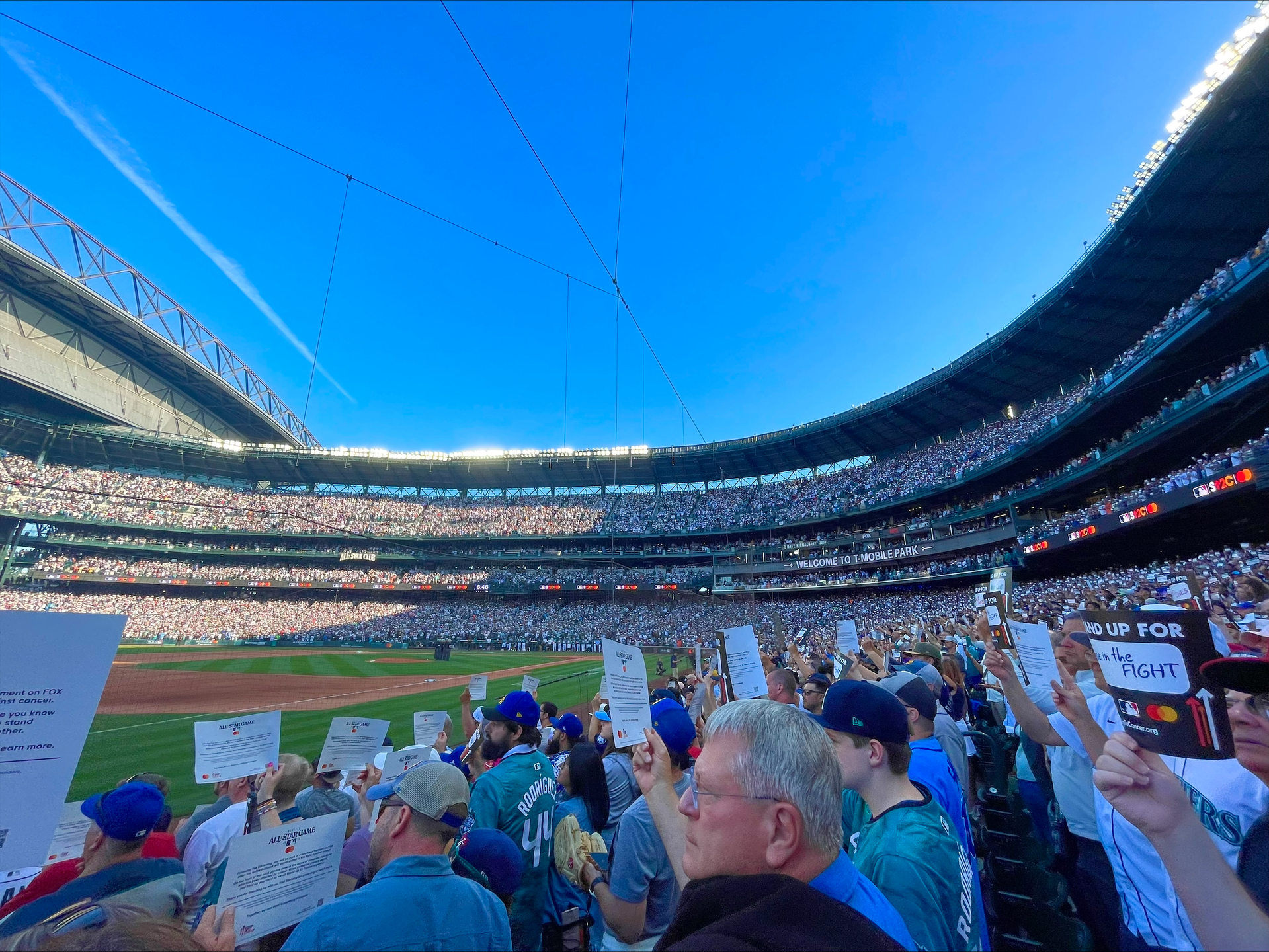 People stand in a baseball stadium holding cards urging people to stand up to fight cancer