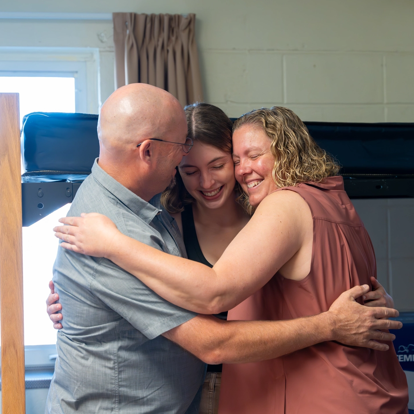 A student and her parents hug in her dorm room.