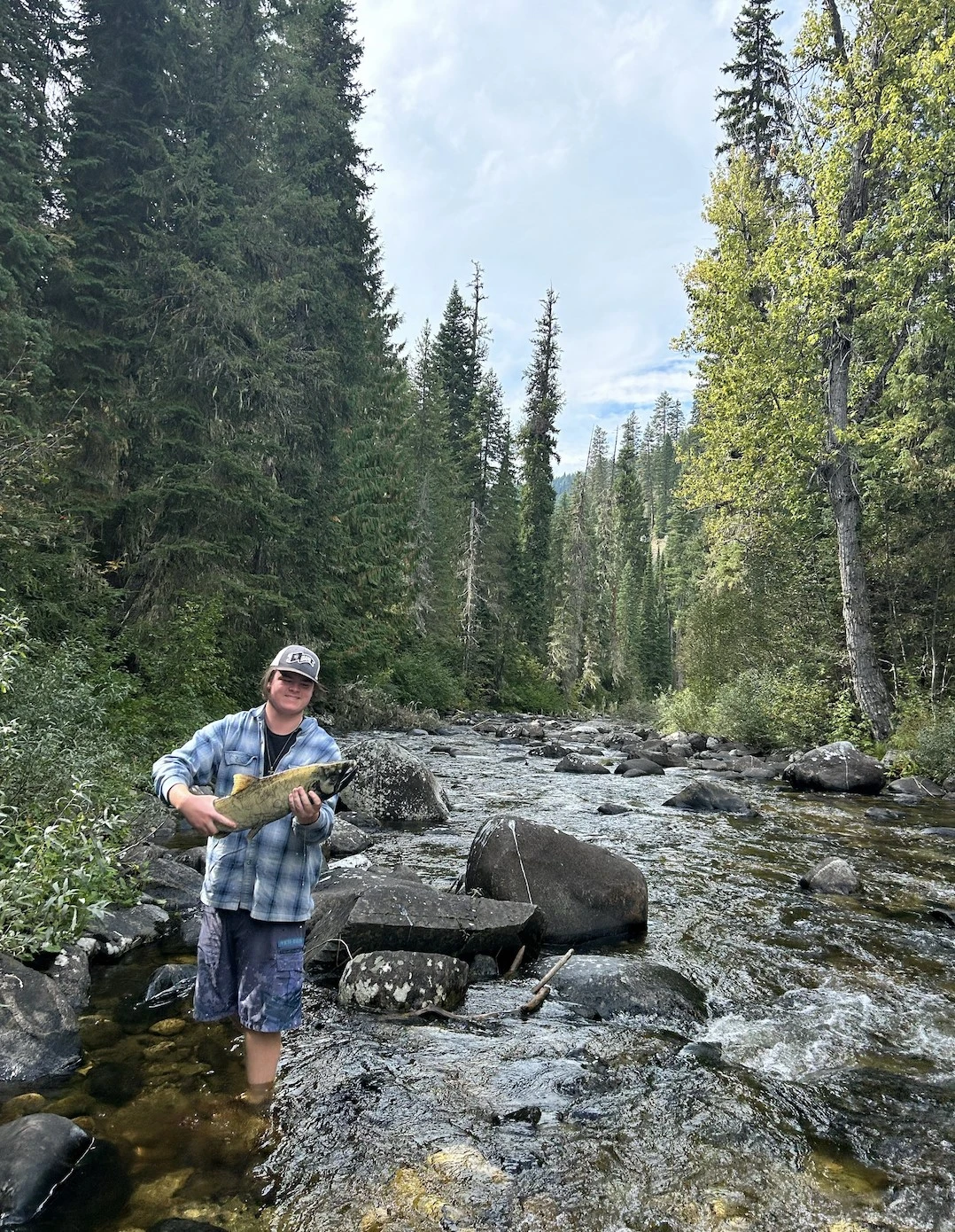 Jack Stafford stands in stream and holds a colorful fish