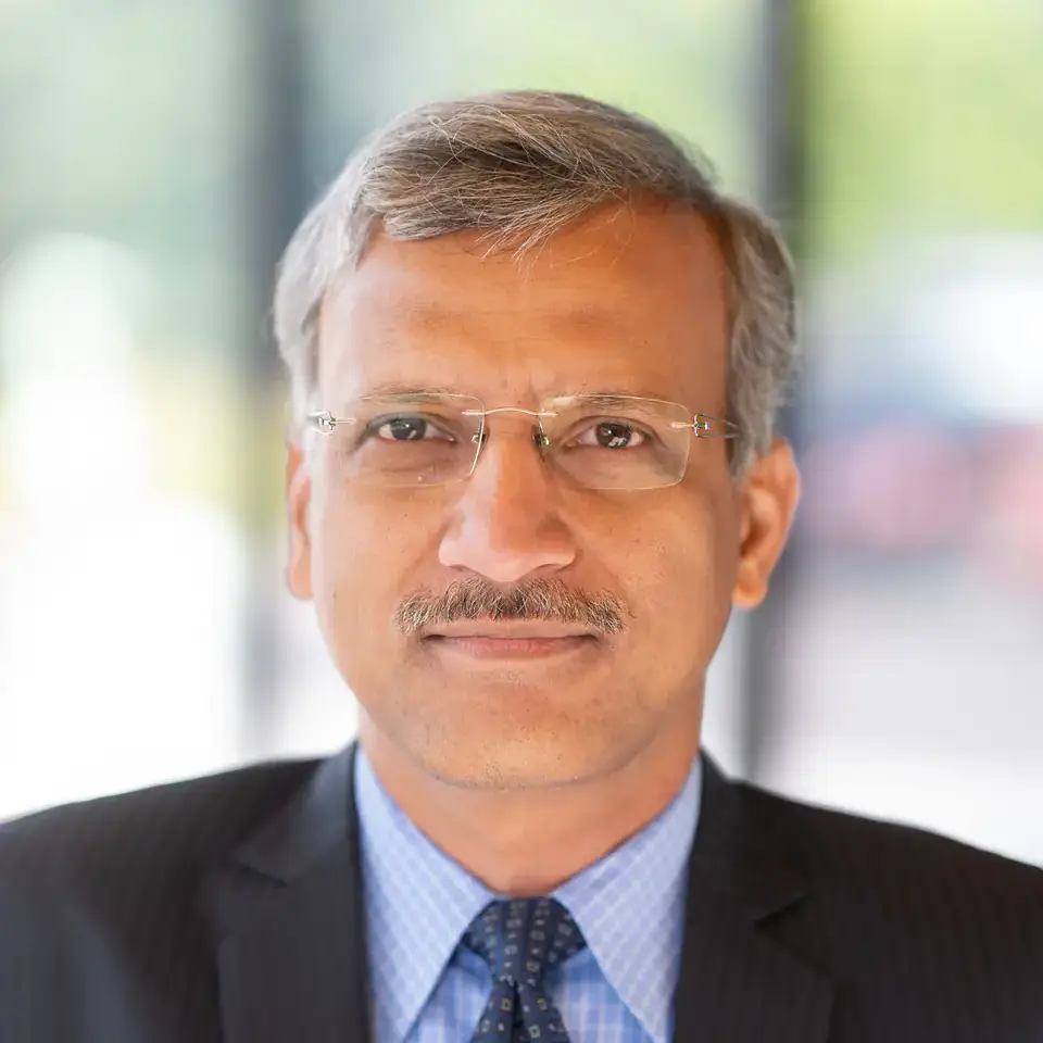 A person in a professional outfit with a blurred outdoor background.