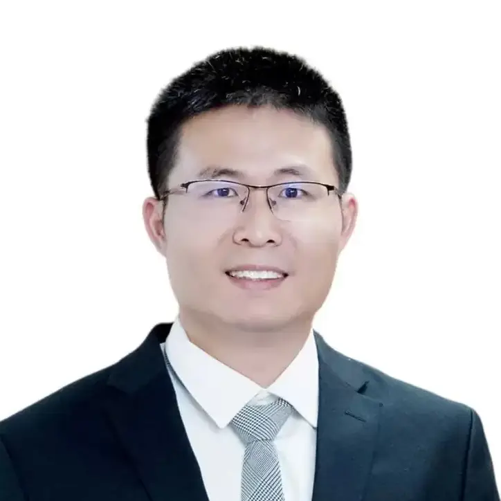 Professional headshot of a smiling man in glasses wearing a dark suit and light tie on a white background