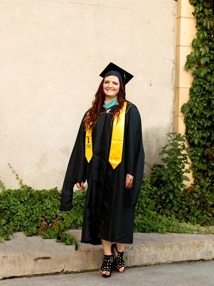 Woman in cap and gown standing in front of building 