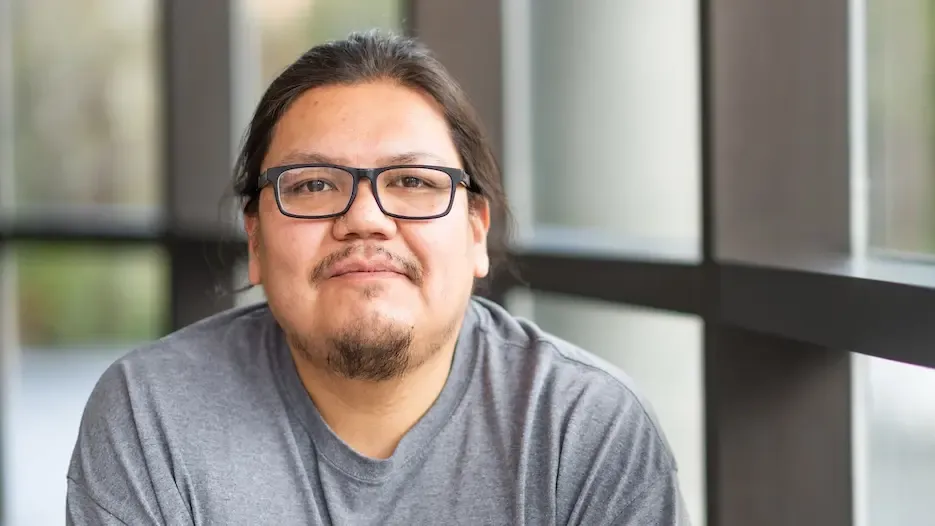 A grinning man with glasses and black hair, wearing a T-shirt.