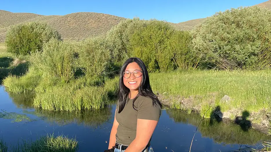 A woman stands in front of a rangeland pond.