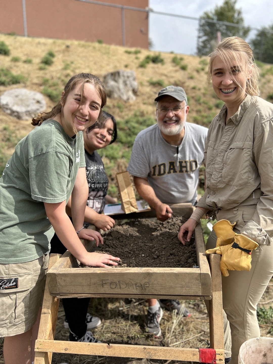 Two U of I students, professor Mark Warner and assistant professor Katrina Eichner stand around a dirt sifter picking through artifacts