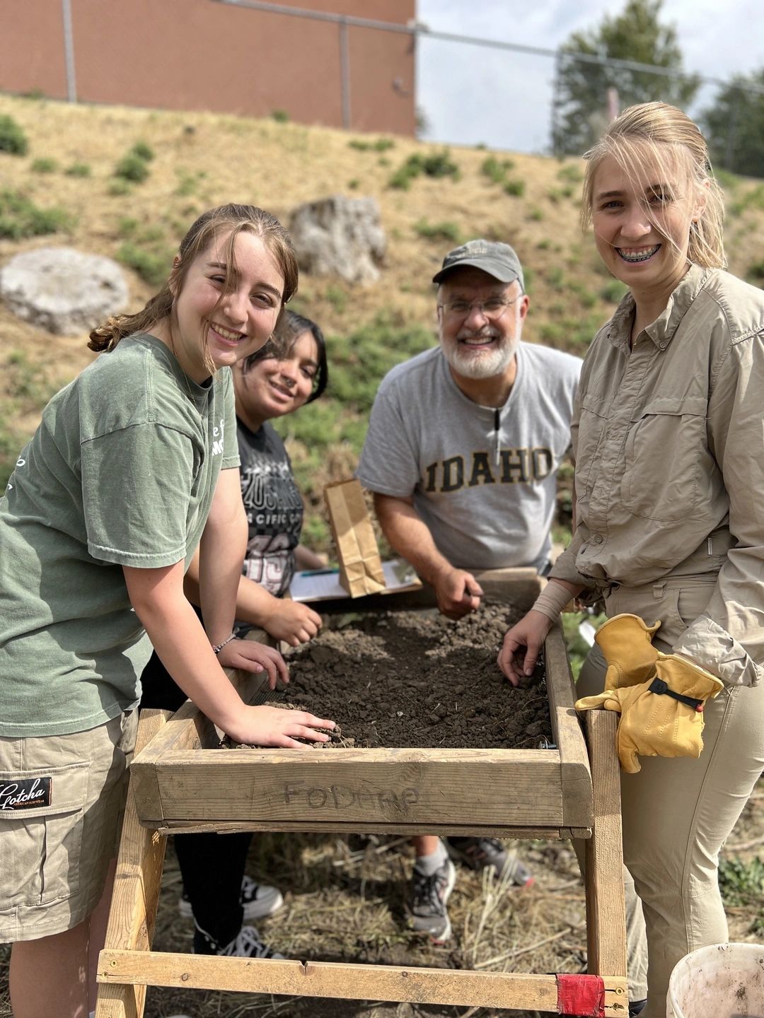 Two U of I students, professor Mark Warner and assistant professor Katrina Eichner stand around a dirt sifter picking through artifacts
