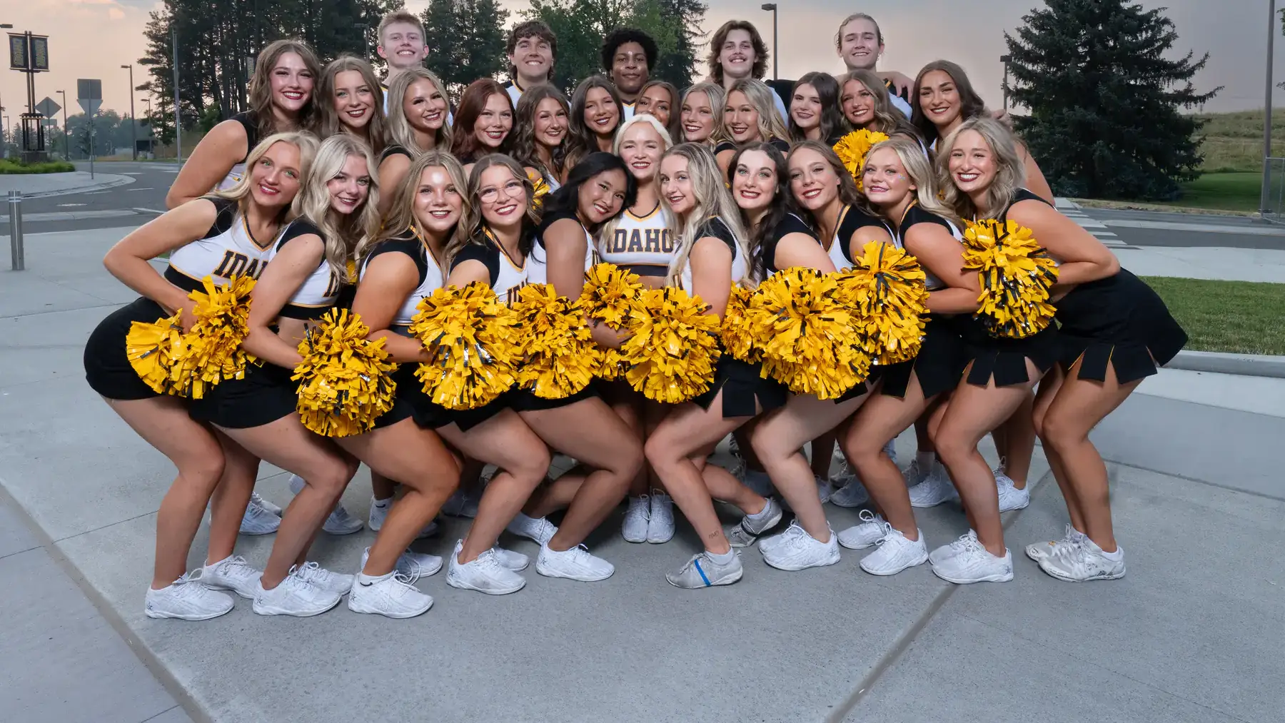 Group photo of the University of Idaho spirit squad dressed in cheer uniforms, posing with pom-poms outdoors on a sunny day.