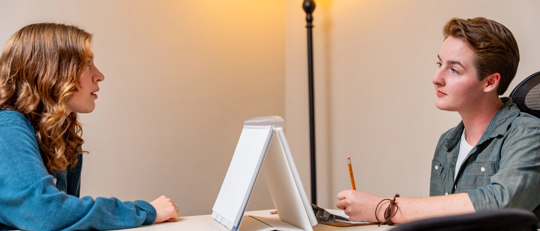 Two people sitting at table with one recording information from conversation