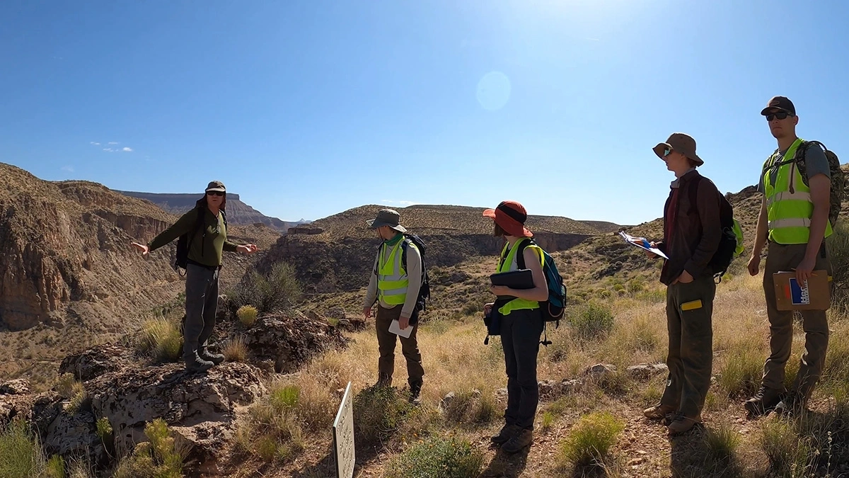 Students listen to a professor who gestures at the rocky landscape surrounding them.