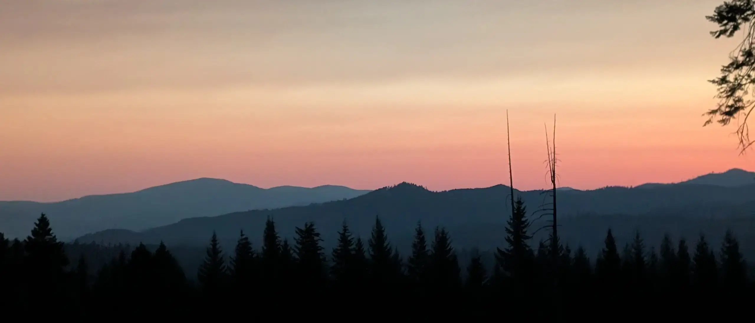 A sunrise with mountains and trees in the distance.