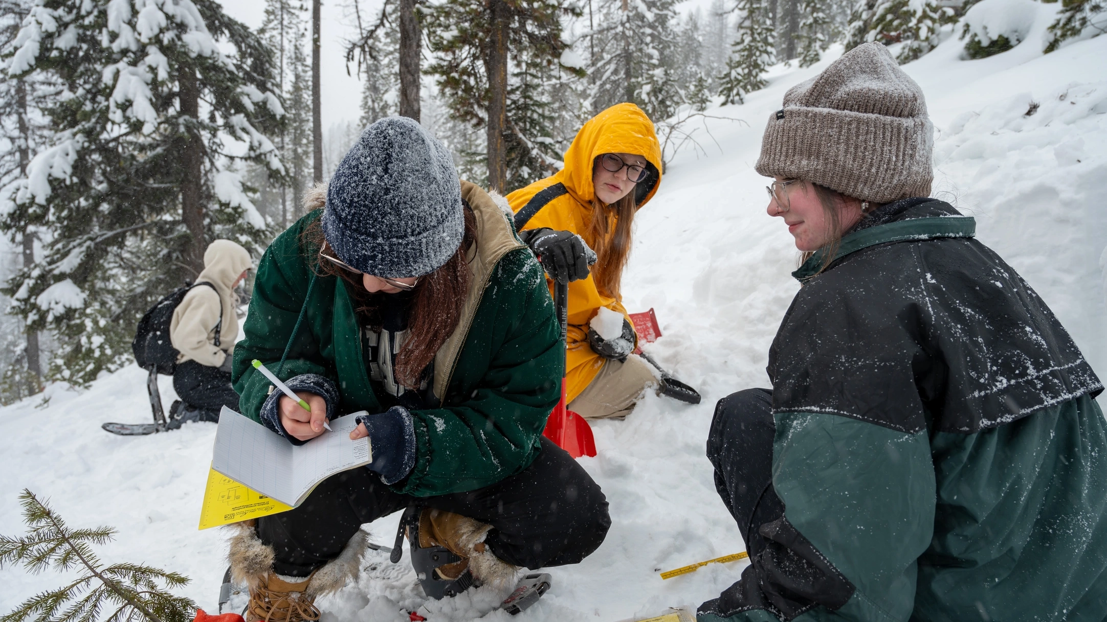 Two students look on as a third student writes in a notebook