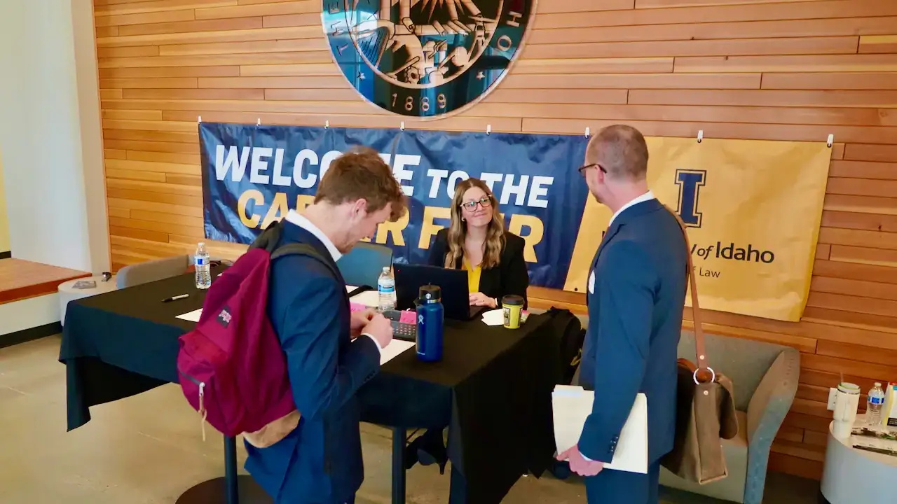 Two men talking to a woman who is sitting behind a check-in desk.