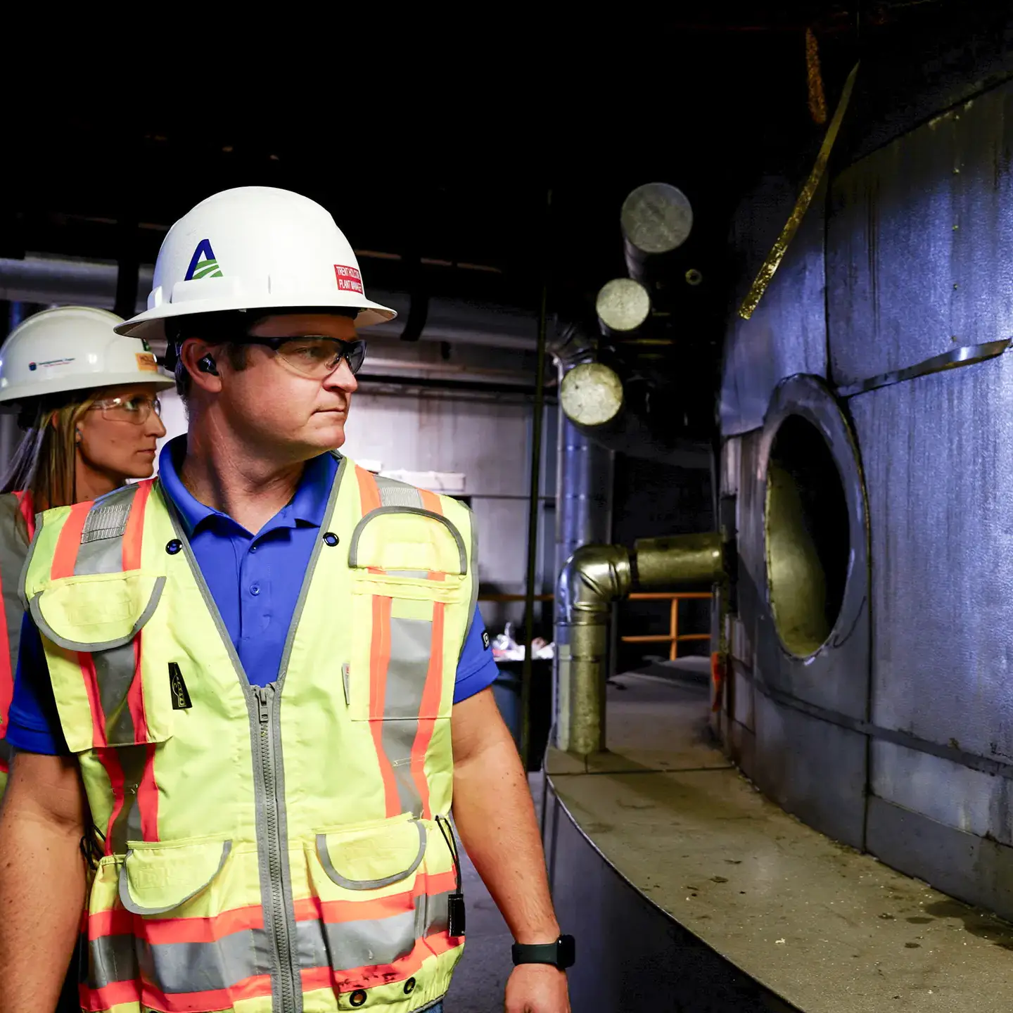 Two factory workers in protective gear surveying factory equipment.