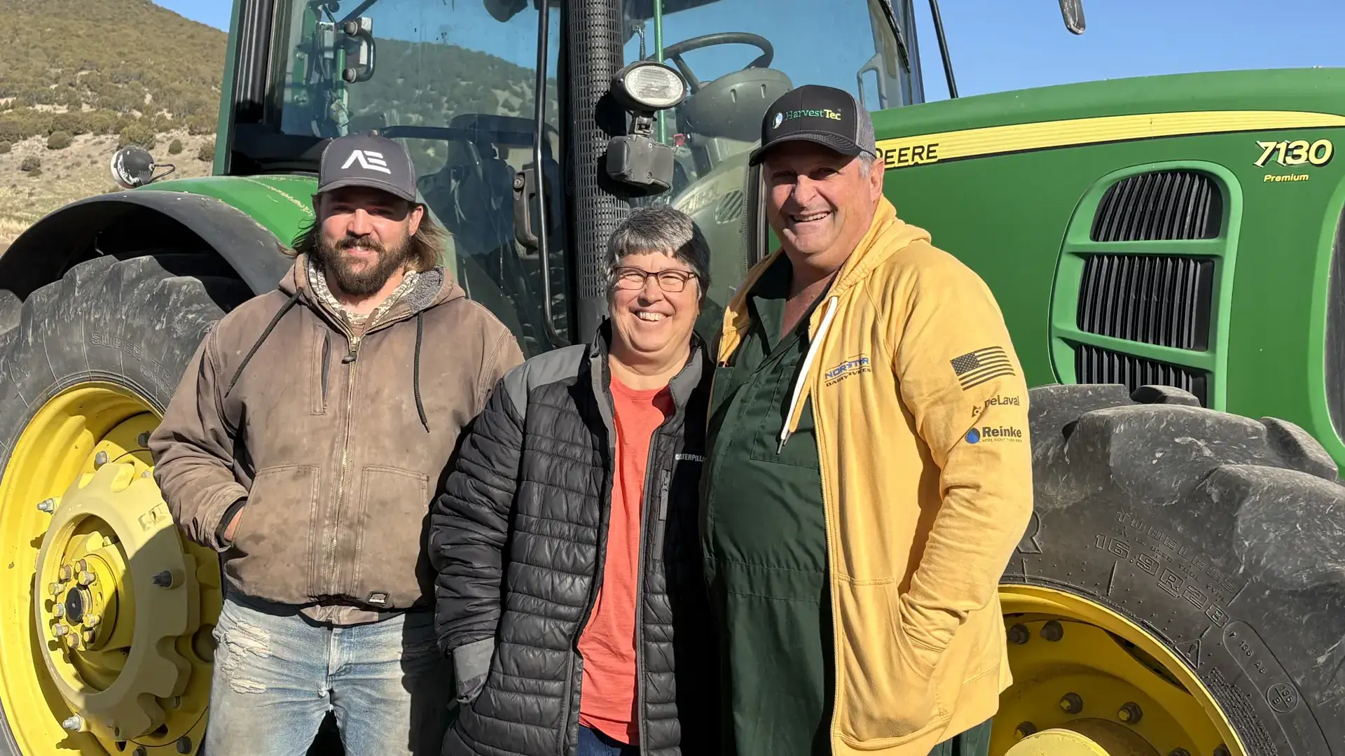 Three people stand in front of a tractor. 