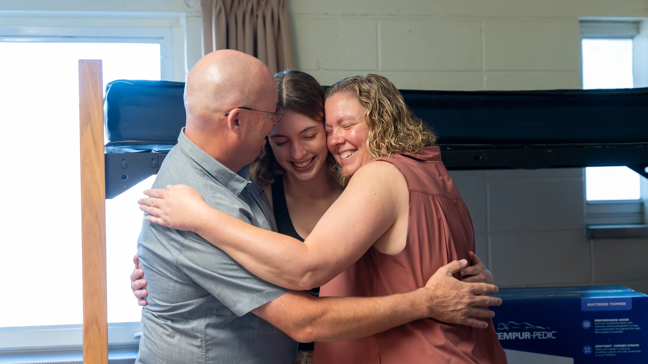A student and her parents hug in her dorm room.