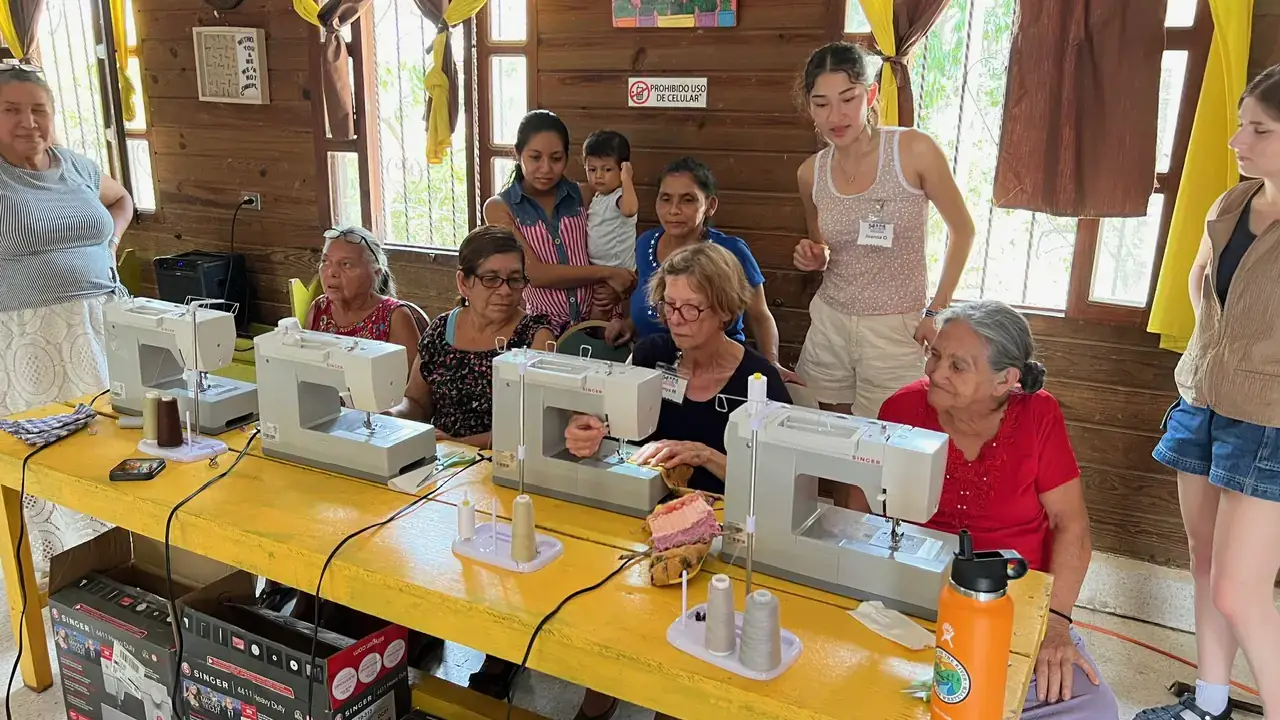 A group of women use sewing machines while others observe.