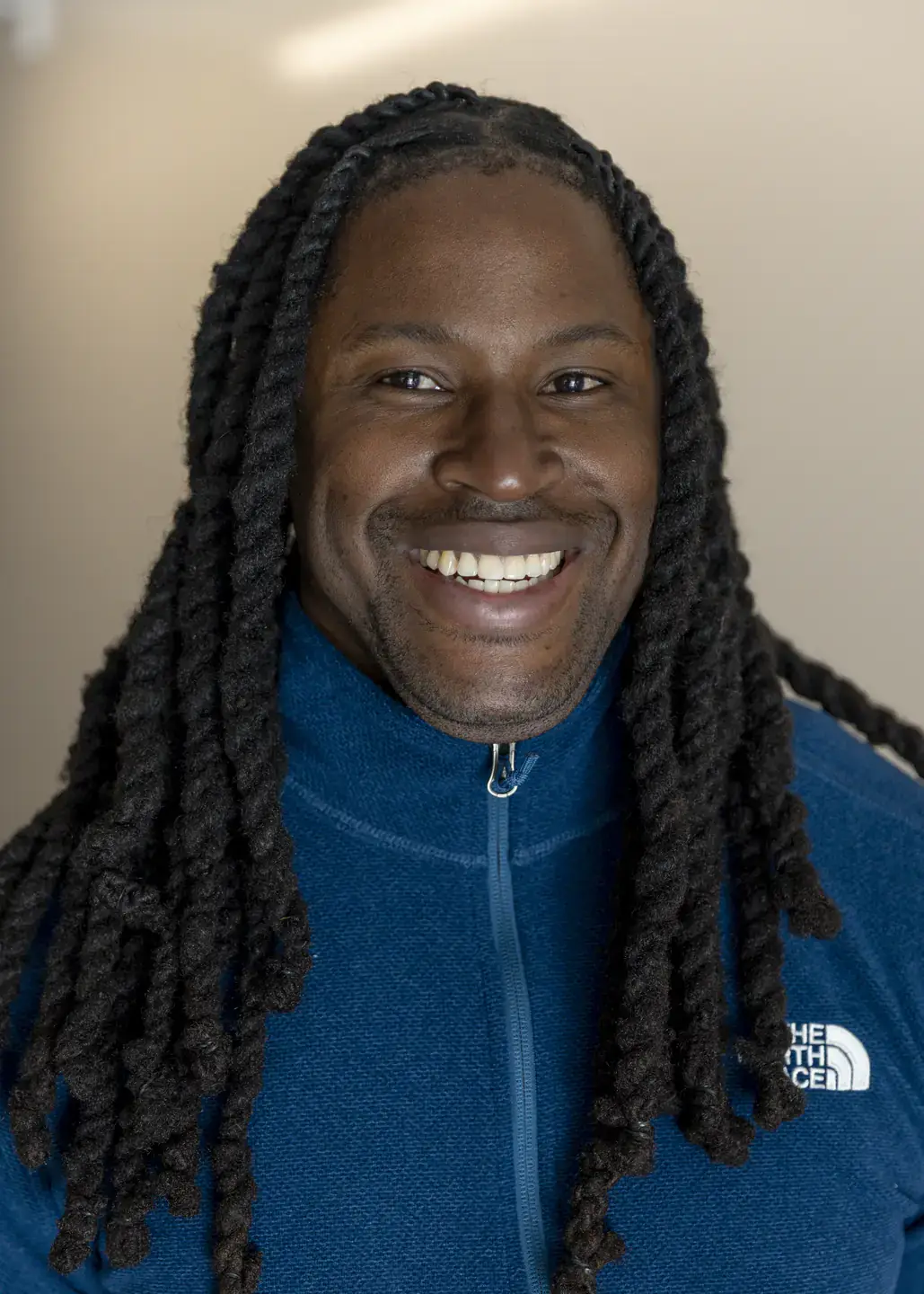 Lorenzo Rene, a black man with long black hair, smiles and wears a blue sweatshirt.
